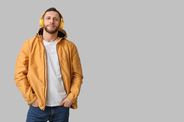 Fototapeta premium Young man in yellow jacket and headphones listening to music, casual fashion and modern lifestyle, isolated on gray background