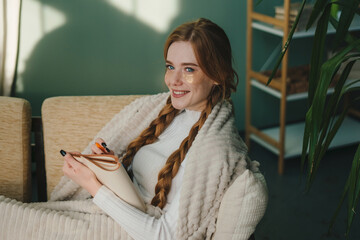 Young woman sitting on the sofa with eye patches under her eyes writing down ideas, making a list...