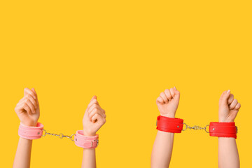 Female hands in handcuffs from sex shop on yellow background, closeup