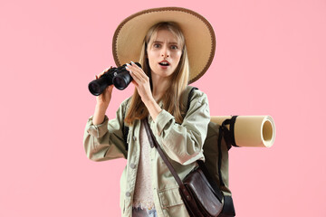 Obraz premium Shocked female traveler with binoculars on pink background
