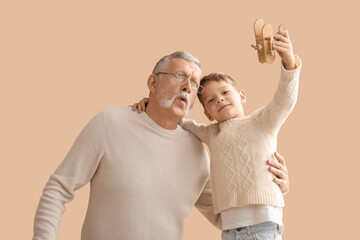 Grandfather and his cute little grandson playing with wooden airplane on beige background
