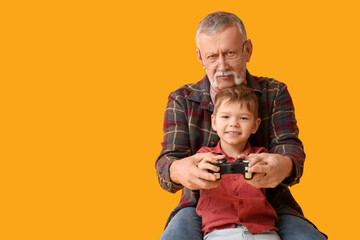Grandfather with his happy cute little grandson playing video games on yellow background