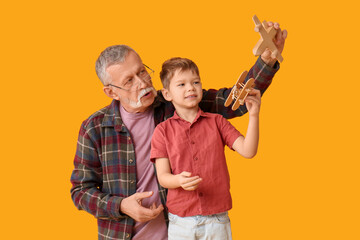 Grandfather and his happy cute little grandson playing with wooden toys on yellow background