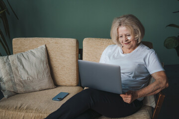 Happy mature retired woman looking at laptop screen for video call with happy mood on sofa at home....