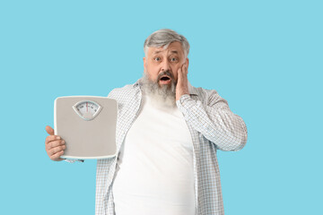 Overweight mature shocked man with scales on blue background. Weight loss concept