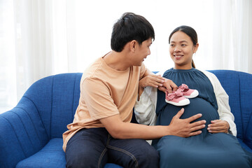pregnant woman with her husband showing small shoes on stomach for newborn baby