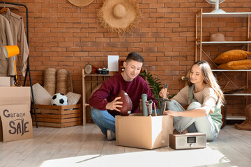 Young couple with box of unwanted stuff in room. Yard Sale