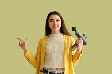 Young woman with percussive massager pointing at something on green background