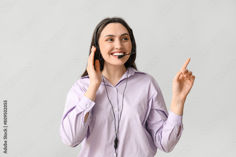Poster female technical support agent in headset pointing at something on grey background