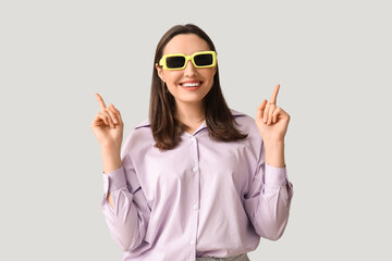 Smiling young woman in sunglasses pointing at something on grey background