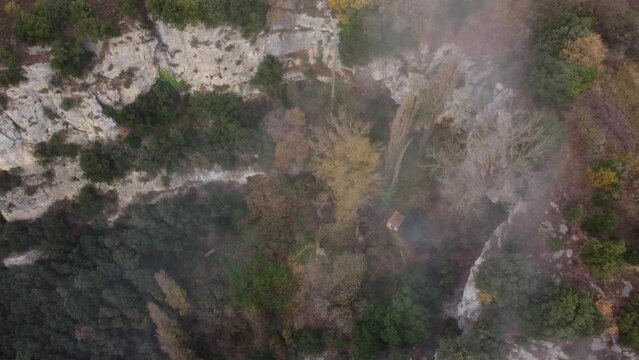 Misty autumn forest and cliffs in osona, barcelona, showing a lone cabin, aerial view