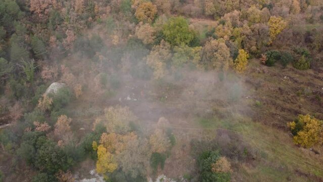 Osona's foggy landscape in autumn, showcasing colorful trees and rocky terrain, aerial view