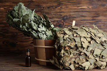 Sauna brooms, bucket and bottle of essential oil on wooden background