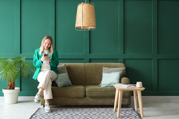 Young woman using mobile phone on sofa in green living room
