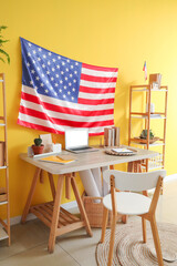 Interior of office with workplace, laptop, chair and USA flag on yellow wall