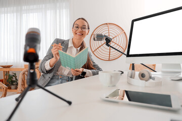 Young woman with notebook recording podcast at table in studio