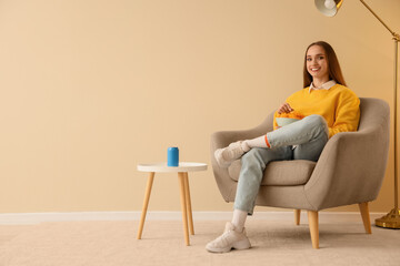 Young woman with potato chips sitting in armchair near beige wall