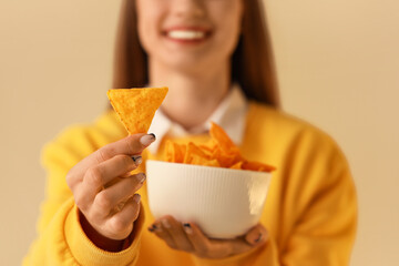 Young woman with bowl of tasty nachos on beige background, closeup