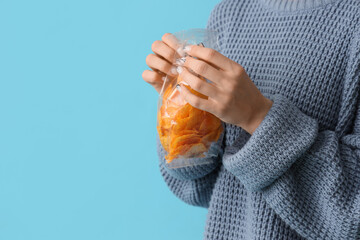 Young woman opening package of potato chips on blue background, closeup