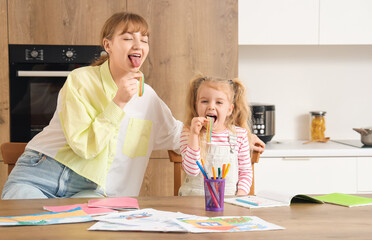 Nanny with little girl eating jelly candies in kitchen
