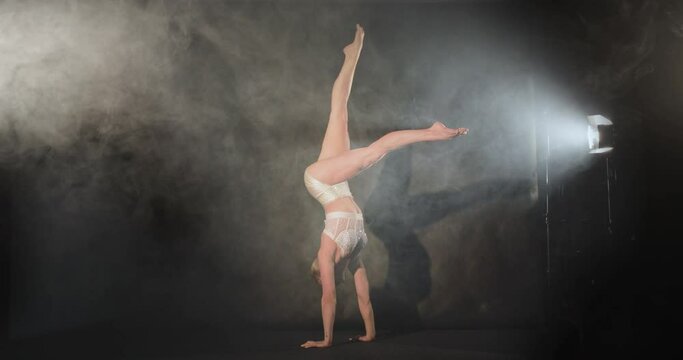 Acrobat performs handstand with leg movements in smoky haze and spotlight