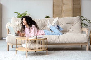 Obraz premium Young African-American woman using laptop on sofa at home