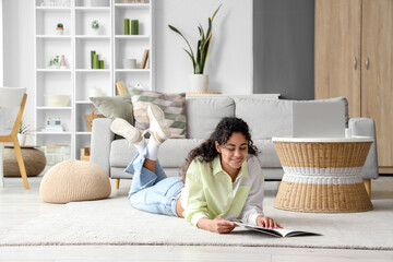 Young African-American woman reading magazine on carpet at home