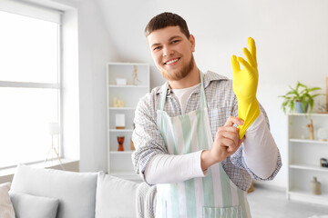 Young bearded man putting on rubber glove before cleaning at home