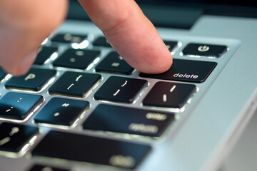 Finger of the computer user, he presses the delete button on the computer keyboard	