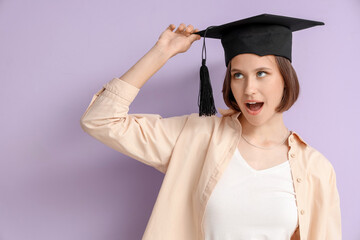 Funny female student in graduation hat on lilac background