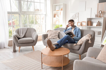 Young tattooed man in headphones reading magazine on sofa at home