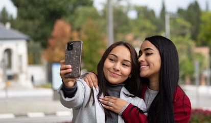 Two smiling lesbian couple latin women are taking a selfie together outdoors