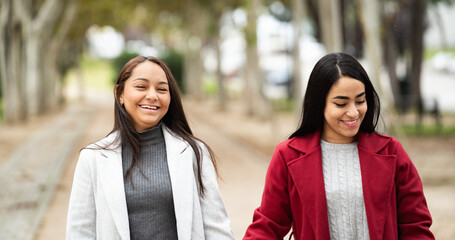 Two women are walking down a path, smiling and laughing. They are wearing coats and seem to be enjoying their time togethe