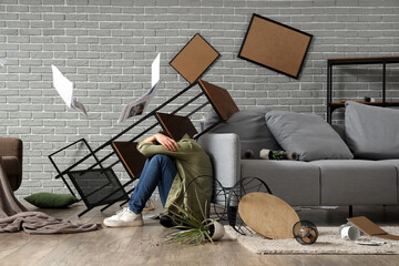 Young woman sitting near sofa during earthquake at home