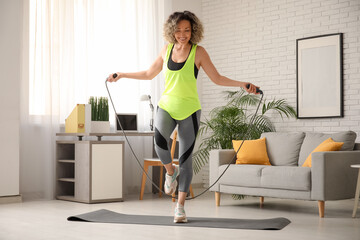 Happy mature sporty woman training with jumping rope at home