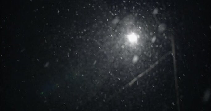 Winter snowfall at night snowing on city street in street light. Snow flakes falling in slow motion in snowstorm.