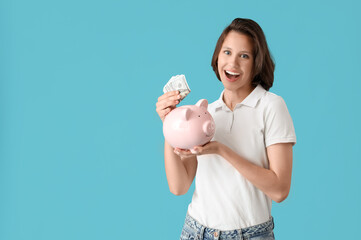 Pretty young woman with money and piggy bank on blue background. Savings concept