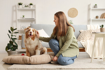 Young woman with cute Australian Shepherd dog on pet bed at home