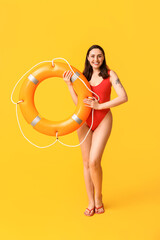 Young female lifeguard with ring buoy on yellow background