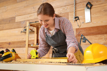 Young female carpenter with measuring tape and plank in workshop. Labor Day celebration