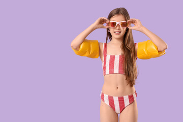 Cute little happy girl in swimsuit with inflatable armbands on purple background