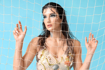 Beautiful young woman dressed as mythical mermaid visible through net on blue background