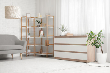 Shelving unit, wooden chest of drawers and houseplants in interior of living room