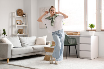 Young woman in eyeglasses and headphones dancing near sofa in living room