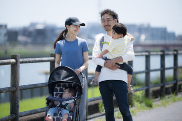 Upper half of a parent and child (family of four) taking a walk in a park along a river in sunny...