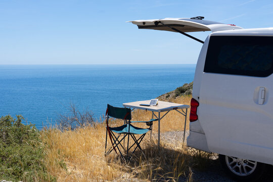 Comper van with a camping table and chair and a mobile phone charging with a solar charger with a sea background