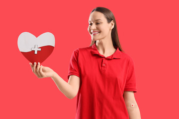 Female blood donor with applied patch and paper heart on red background