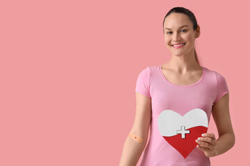 Female blood donor with applied patch and paper heart on pink background