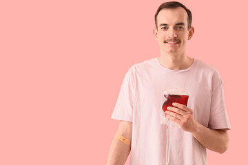 Male blood donor with applied patch and pack for transfusion on pink background