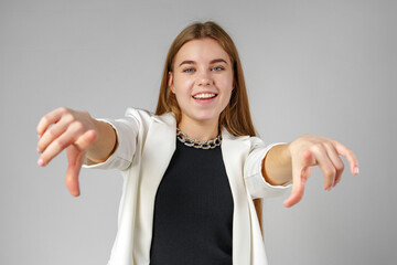 Young Woman in White Blazer Pointing at You Against a Grey Background